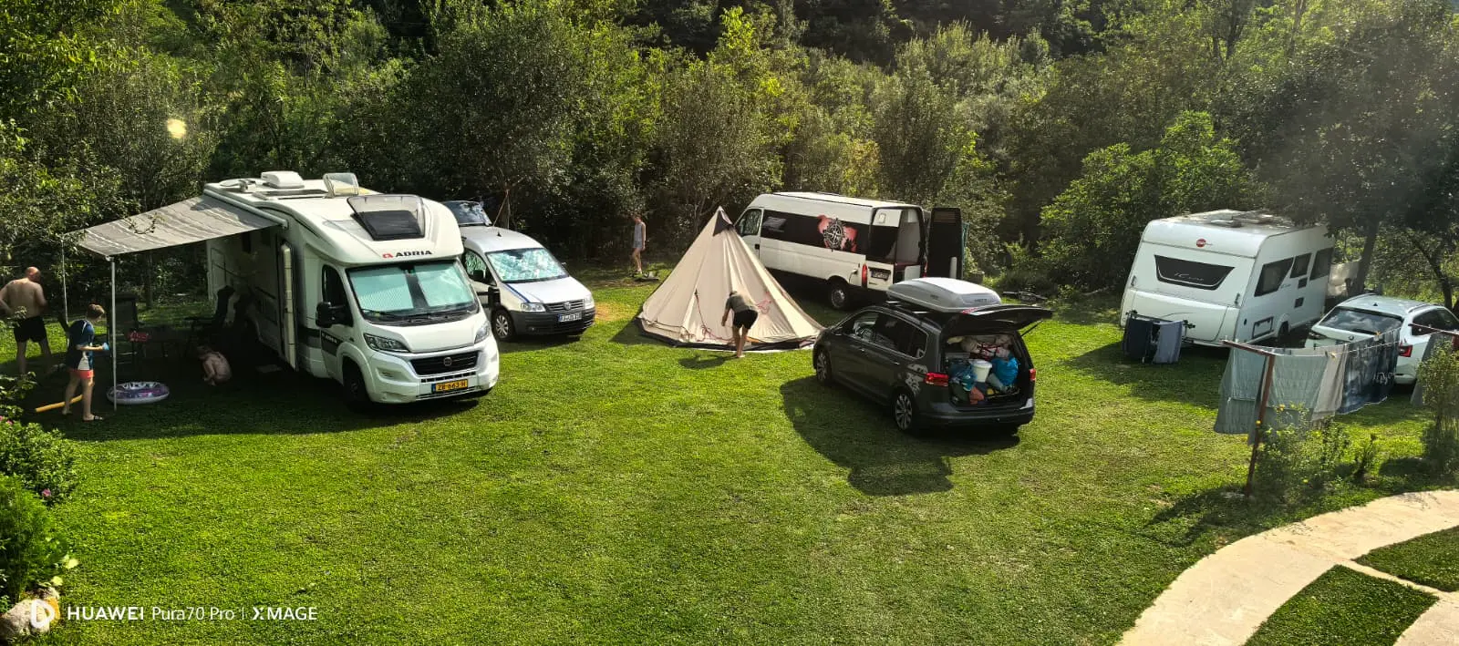 Kamp vozila, kombiji i šator na travnatoj livadi Ravna Campinga, okruženi šumom