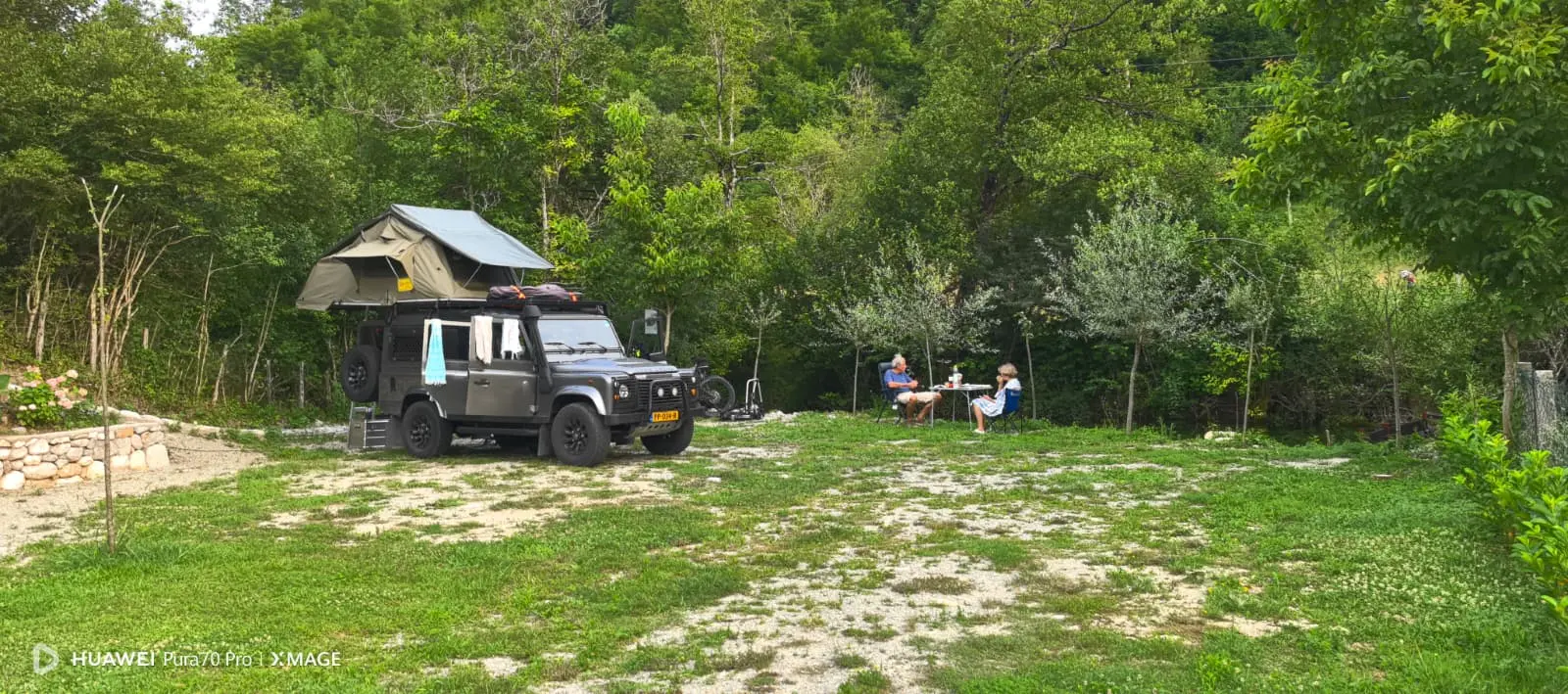 Terenac sa krovnim šatorom i gosti za stolom na parceli uz rub šume