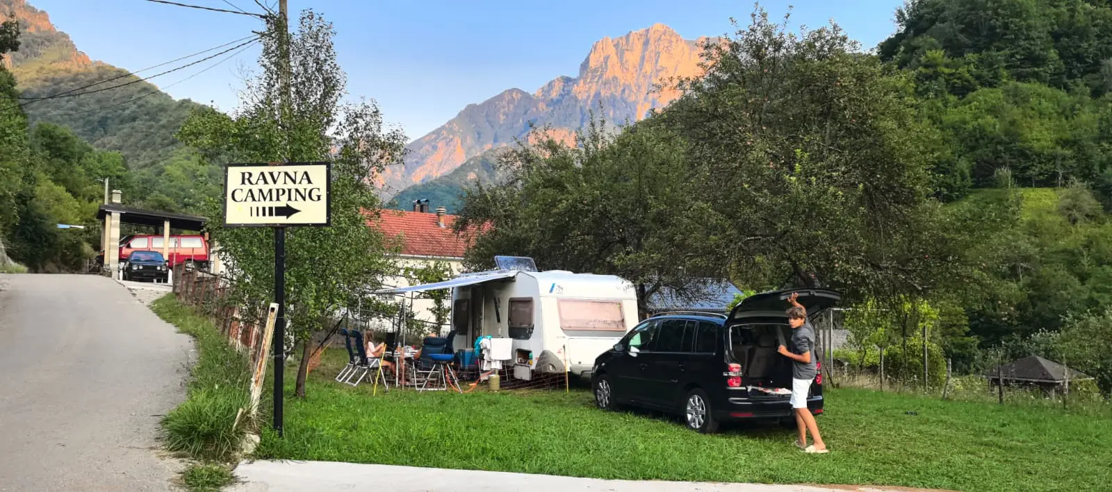 Tabla Ravna Camping uz put, prikolica i vozilo na livadi, vrhovi Prenja obasjani zalaskom sunca