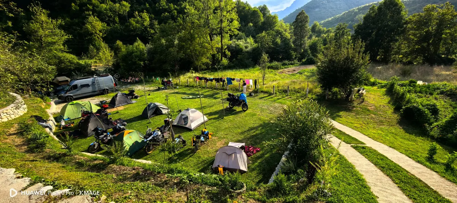 Šatori, motocikli i kamp vozilo na zelenoj livadi Ravna Campinga, okruženi šumovitim padinama